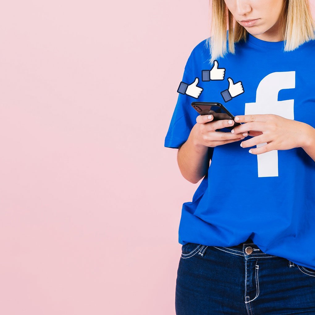 photo représentant une jeune femme utilisatrice de l'application Facebook sur son smartphone et portant un T-shirt à l'effigie de Facebook